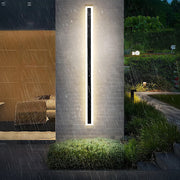 Long black xura linear LED outdoor wall light installed on a textured pillar in the rain, demonstrating IP65 waterproofing