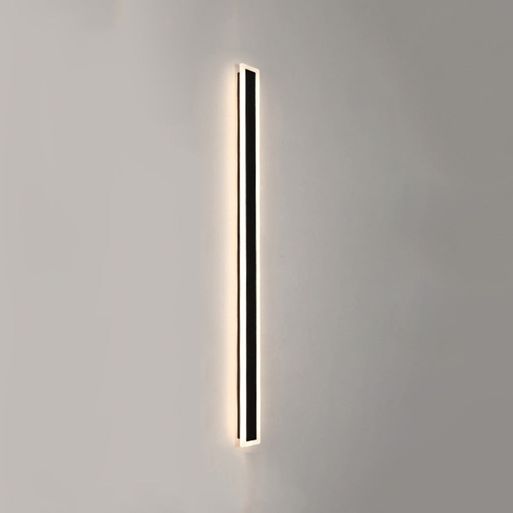 Minimalist long black xura LED wall light glowing vertically on a plain grey exterior wall