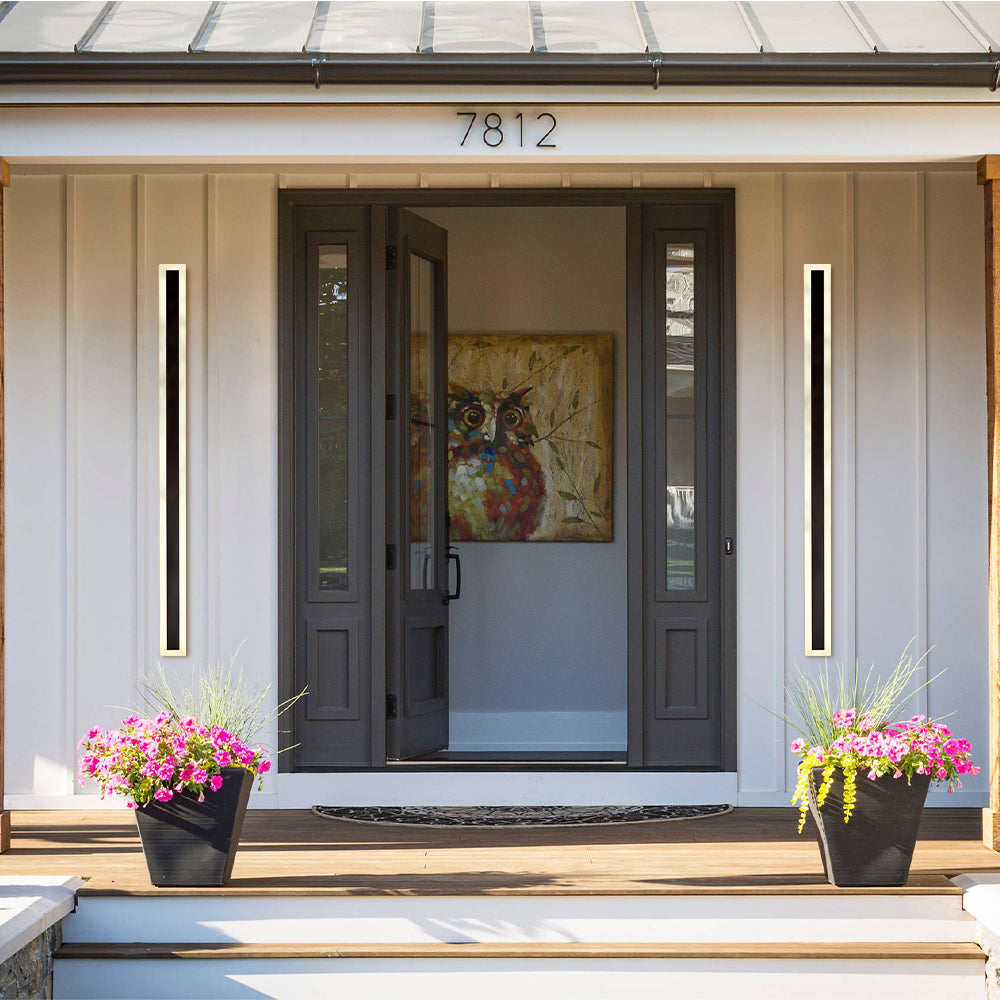Pair of long xura linear LED sconces framing a classic white porch entryway with floral planters