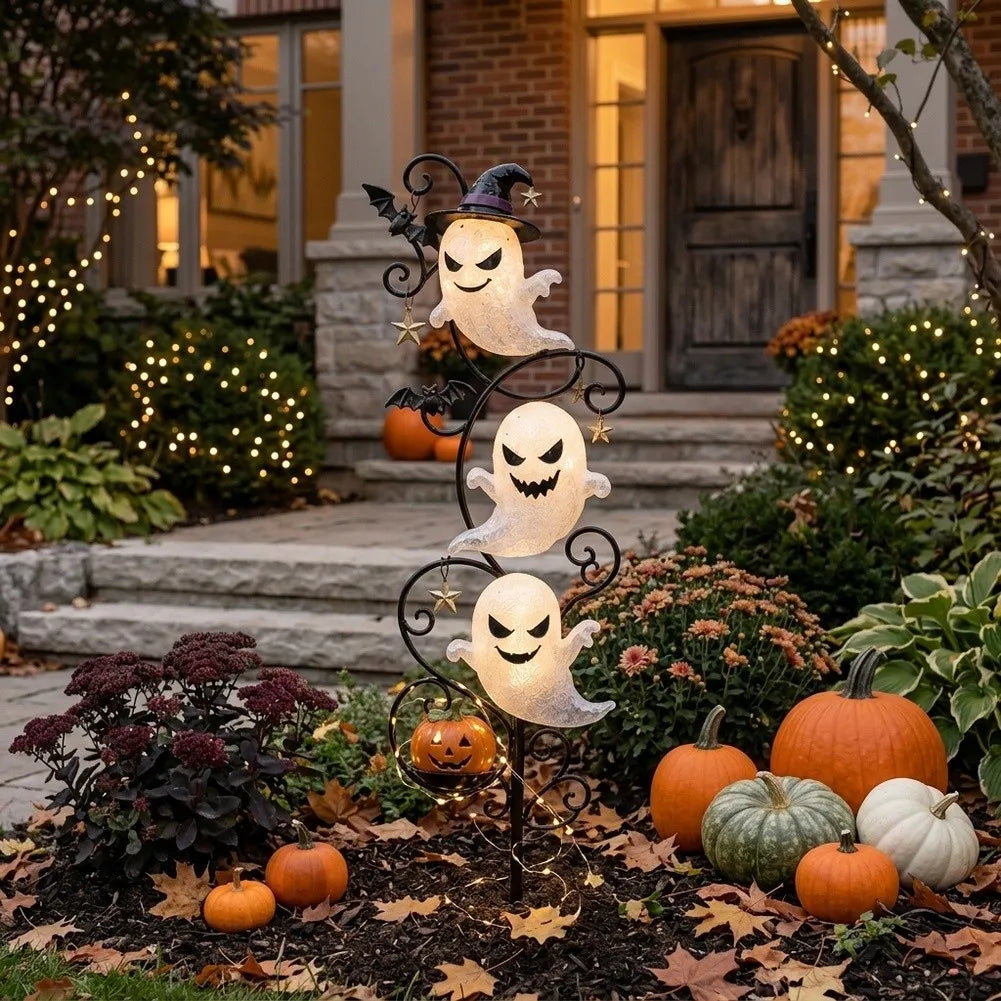 Yardmarker LED ghost garden stake glowing in a garden bed beside a brick porch with string lights and pumpkins