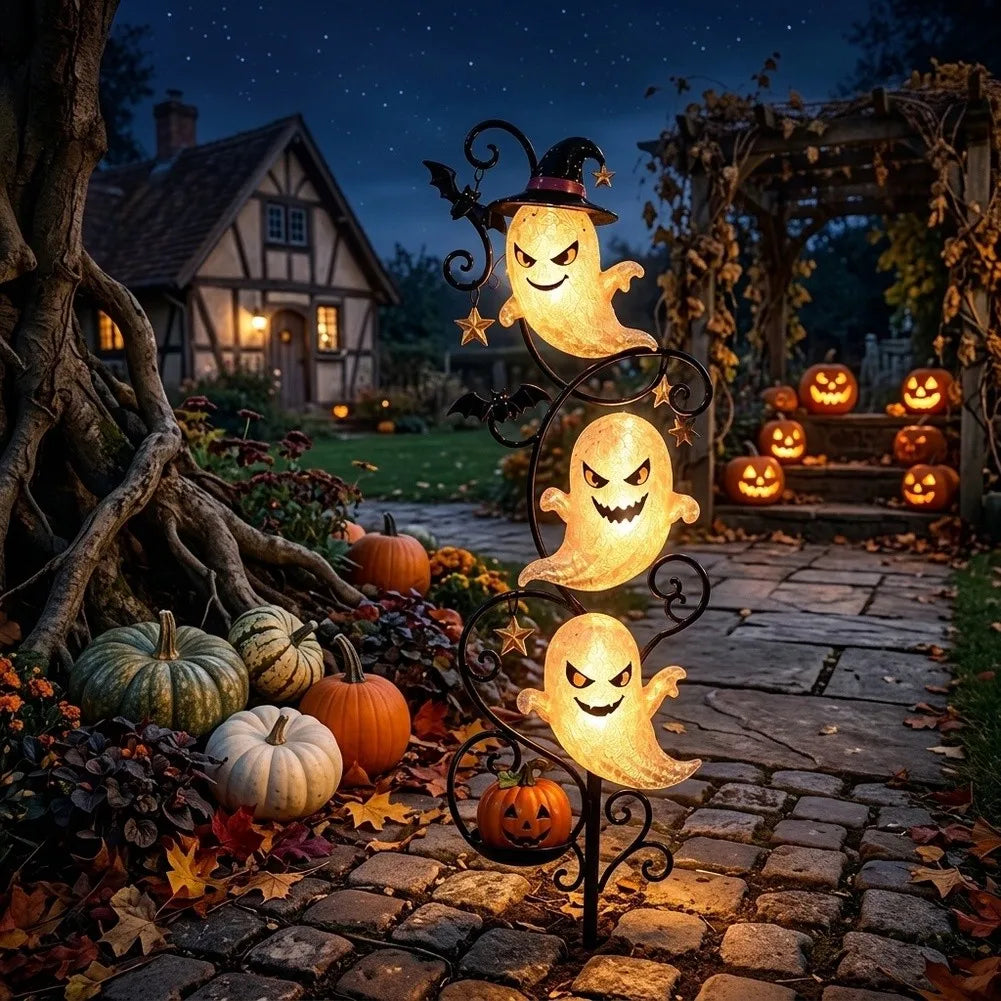 Yardmarker LED glowing ghost garden stake staked in a garden bed with a cottage and jack-o'-lanterns in the background