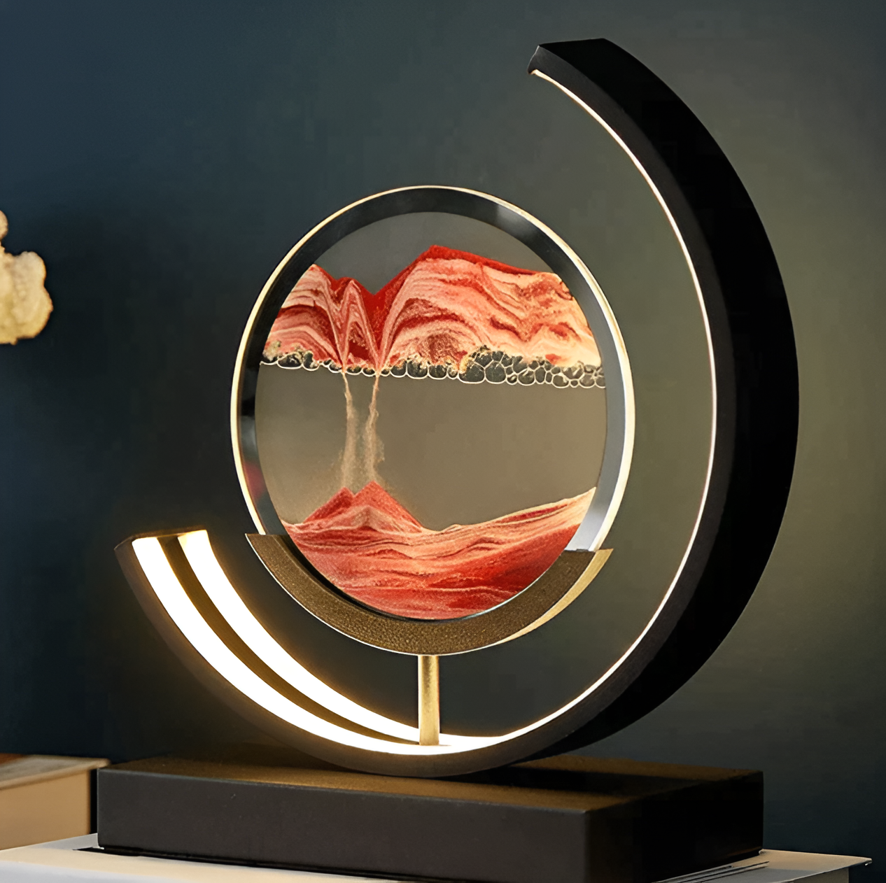 Illuminated black LED quicksand youj art lamp with orange sand creating a dynamic mountain landscape in a dark room