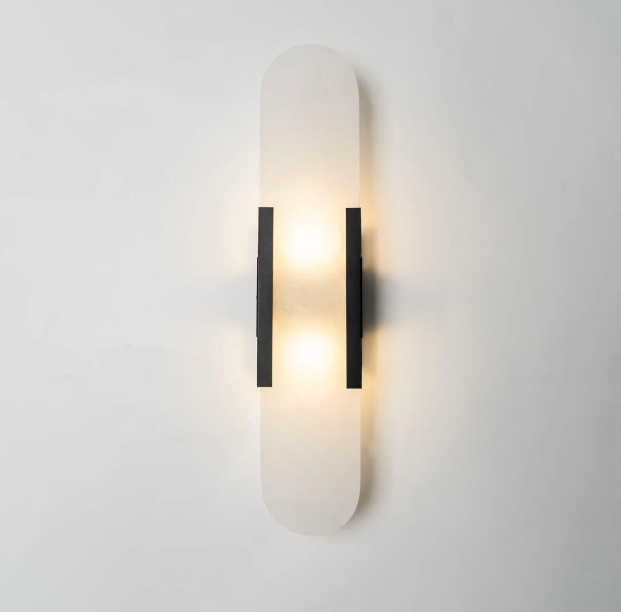 yuhy front view of the modern black hardware and natural marble pill sconce glowing softly